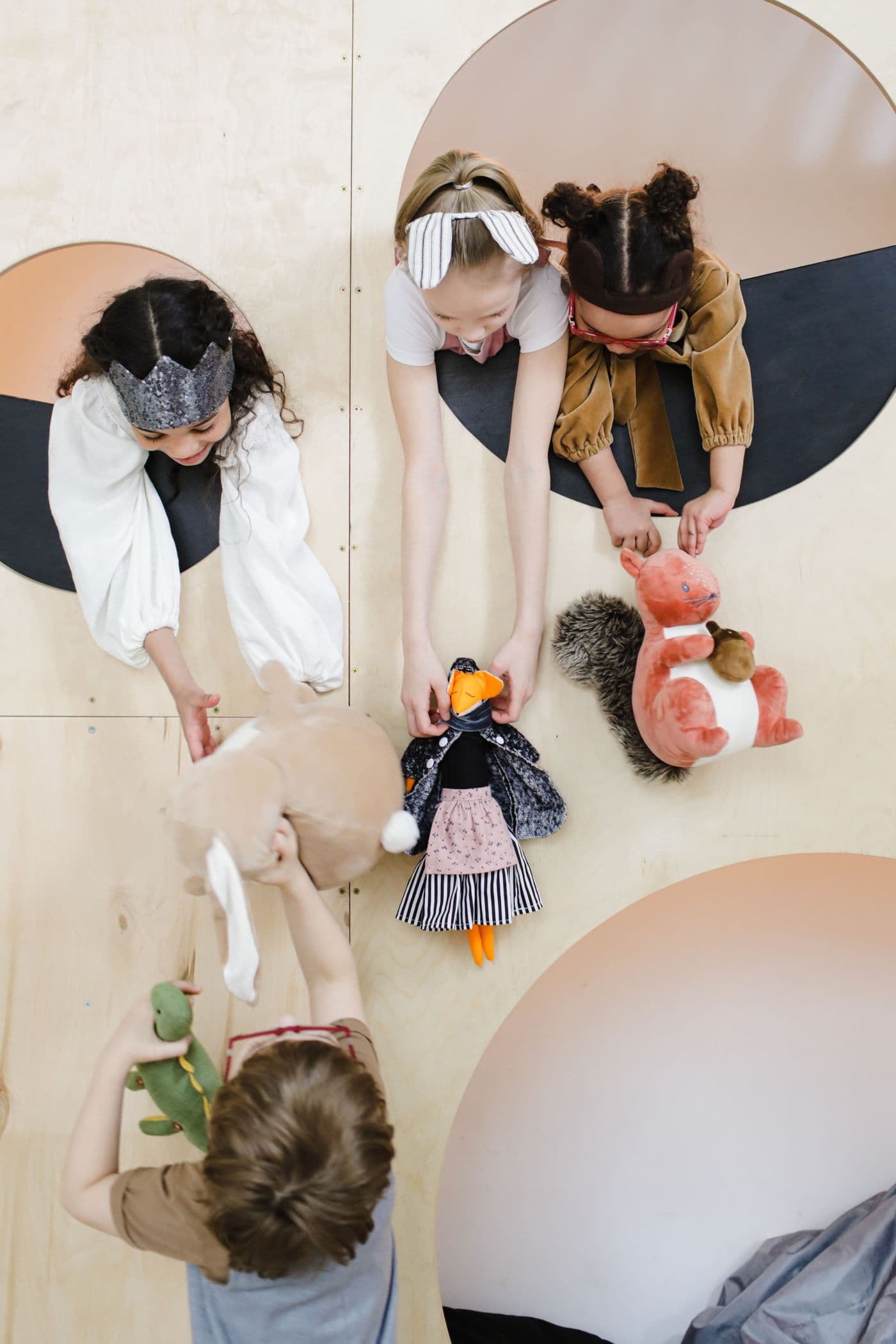 Overhead view of four young children playing together with soft toys on a wooden floor