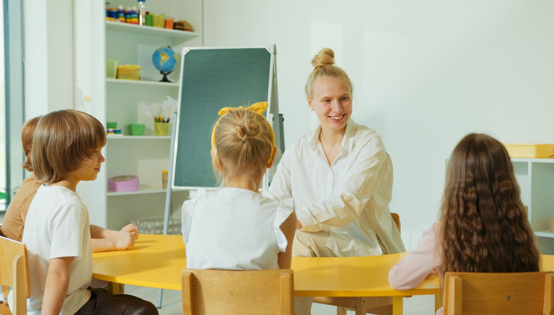 A teacher sitting with three young children around a low classroom table