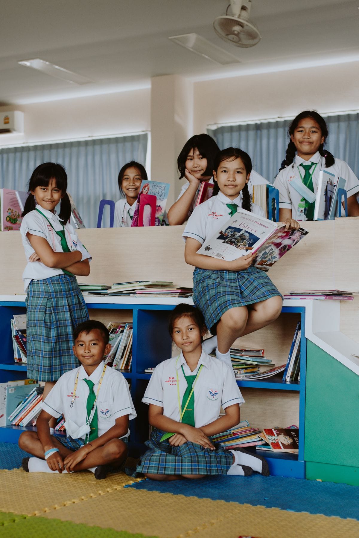 A group of primary students in school uniform together among books in a reading room