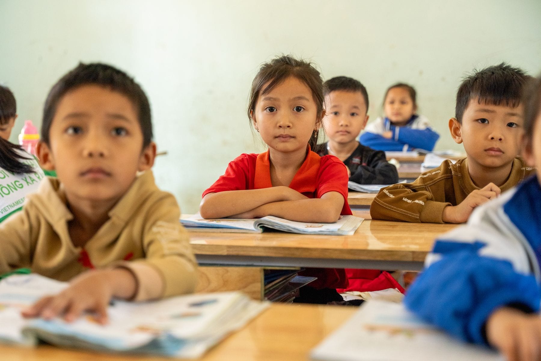 Primary-age children at their desks with open books, listening during a lesson